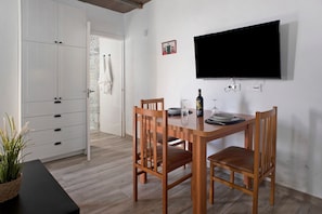 A dining area with a wooden table, chairs, a TV mounted on the wall, and a white cabinet with drawers.