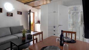 A room with a sofa, a dining table with chairs, a potted plant, a wine bottle, and a wine glass.