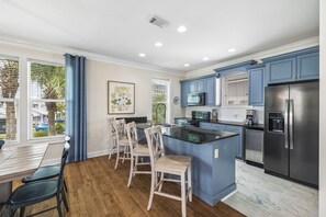A modern kitchen with a central island, blue cabinets, and a stainless steel refrigerator. - Gulf View Home | Steps to Beach Access (Santa Rosa Beach)