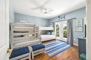 A room with bunk beds, a ceiling fan, a window with curtains, and a striped rug.