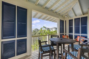 A covered outdoor area with a wooden table and chairs, surrounded by dark shutters.
