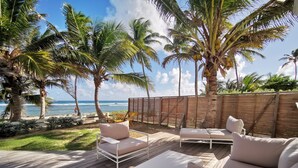A wooden deck with outdoor furniture, palm trees, and a view of the ocean.