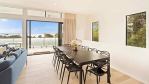 Un comedor moderno con una mesa grande y sillas, ventanas amplias con vistas, y un sofá al frente.