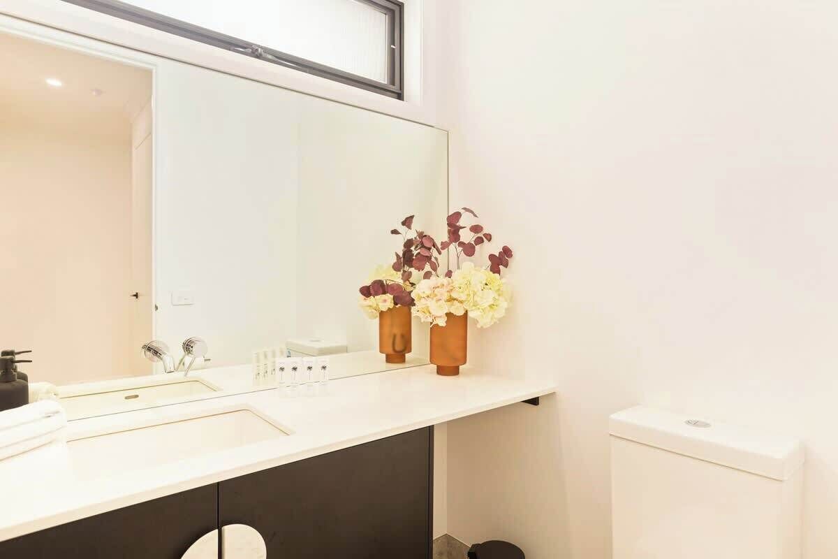 A bathroom with a white sink, two mirrors, and two flower vases.