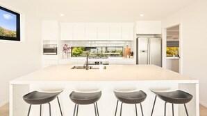 Una cocina moderna con una isla grande, taburetes de bar y vistas a la vegetación.