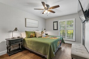 Un dormitorio con cama, lámparas de noche, ventilador de techo, ventana con persianas y una obra de arte colgada en la pared.