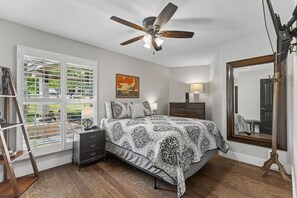 Une chambre à coucher comprenant un lit, une commode, une table de chevet et un ventilateur de plafond.