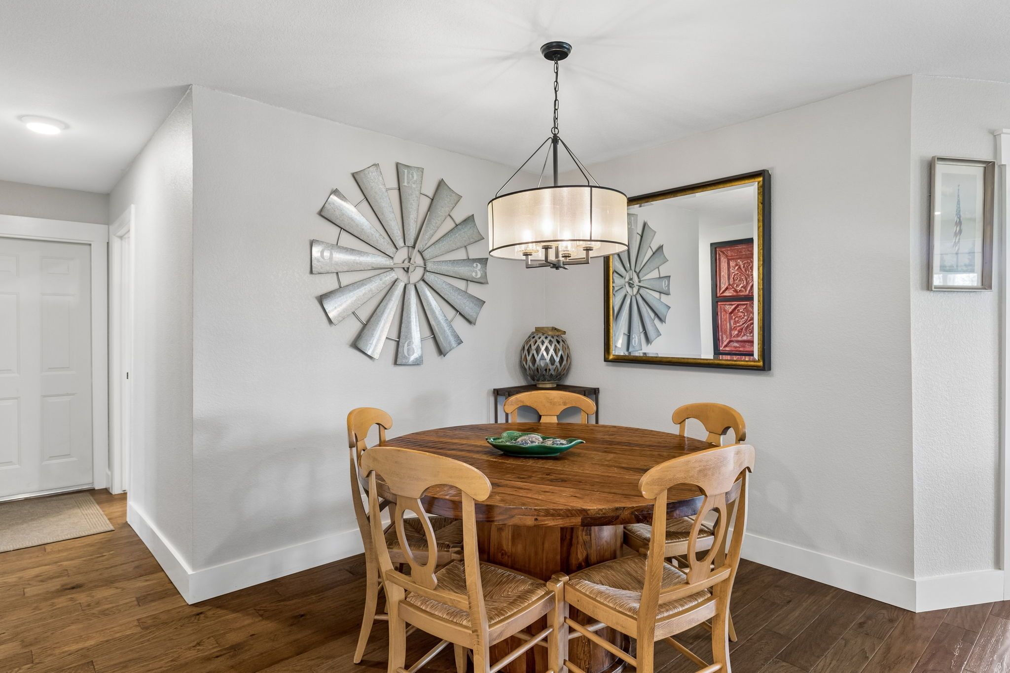 A dining area with a round wooden table, four chairs, a chandelier, and decorative wall art.