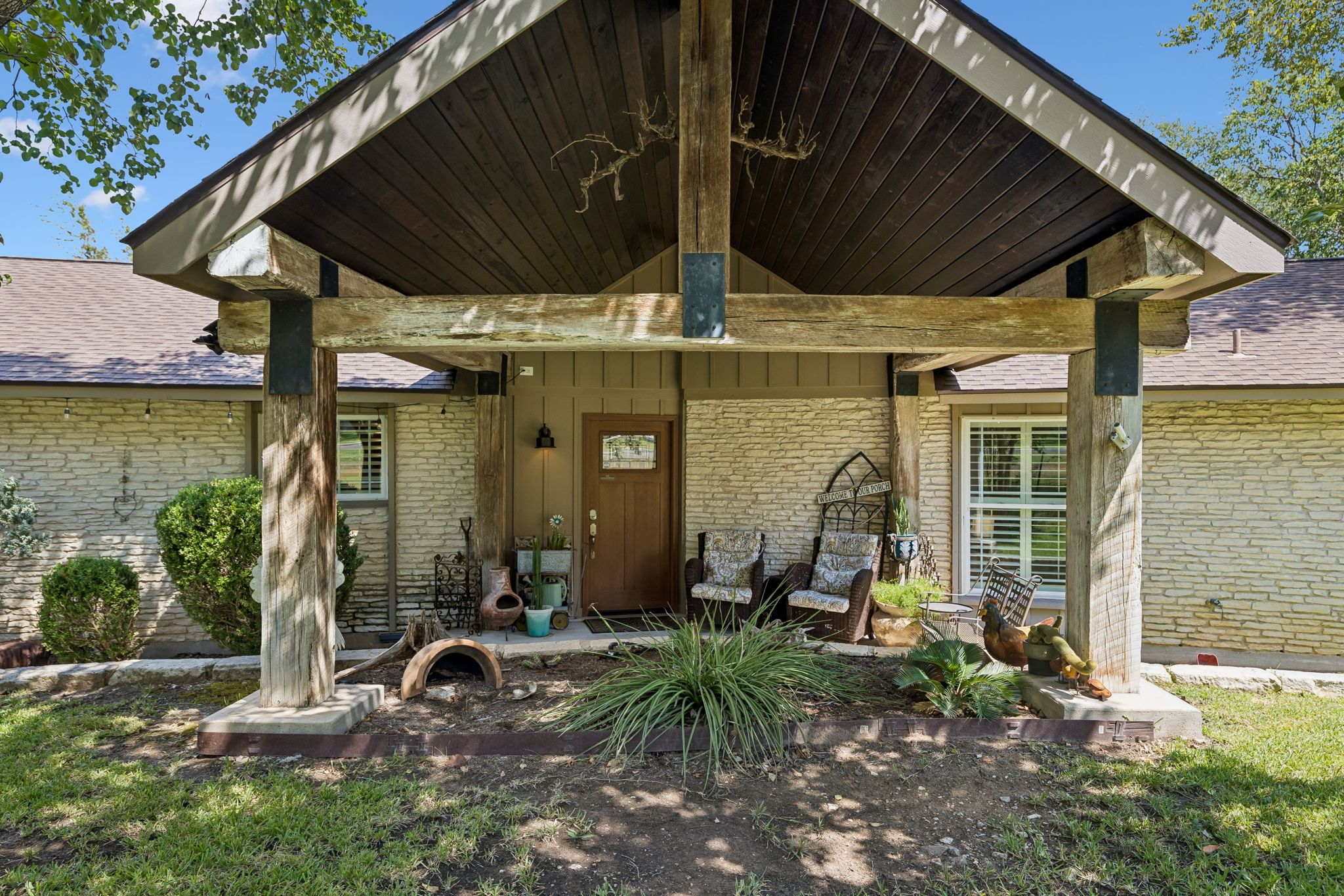A covered porch with a stone wall, a wooden door, and outdoor furniture.