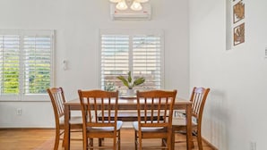 A dining area with a wooden table and chairs, large windows with blinds, and a ceiling-mounted air conditioning unit. - Light & Bright Spanish-Style Beauty, 3 min to Zoo! (San Diego)