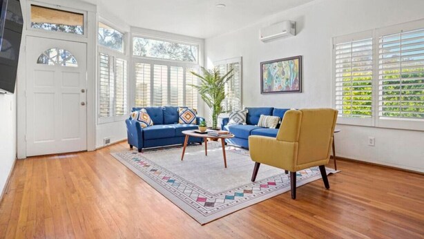 A spacious living room with hardwood floors, a blue sofa, a yellow armchair, a coffee table, and a ceiling fan. - Light & Bright Spanish-Style Beauty, 3 min to Zoo! (San Diego)