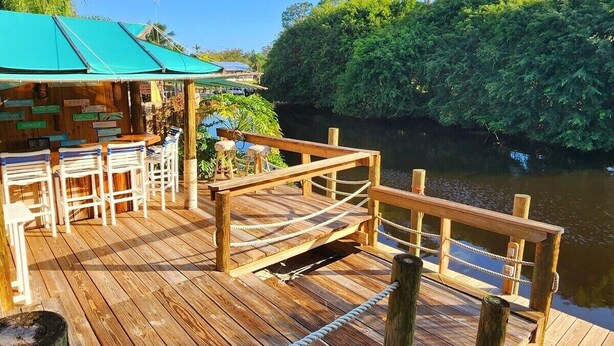 A wooden deck with a rope barrier, a covered seating area, and a view of a river.
