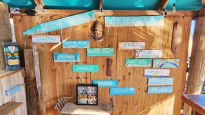 A wooden deck with a metal table and chairs, surrounded by wooden walls with signs pointing to various destinations like the Bahamas, Jamaica, and Puerto Rico.