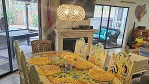 A dining area with a large round table, chairs, and a hanging light fixture.