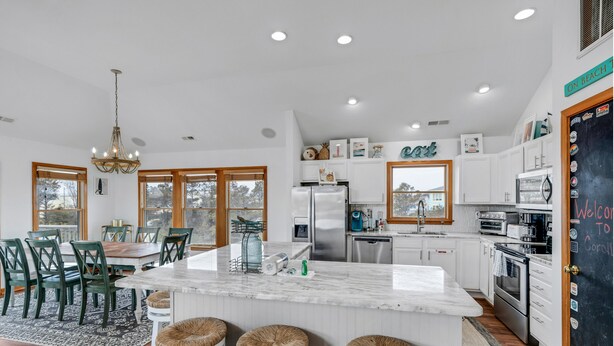 A modern kitchen with white cabinets, a marble island, and a dining area with green chairs and a chandelier.