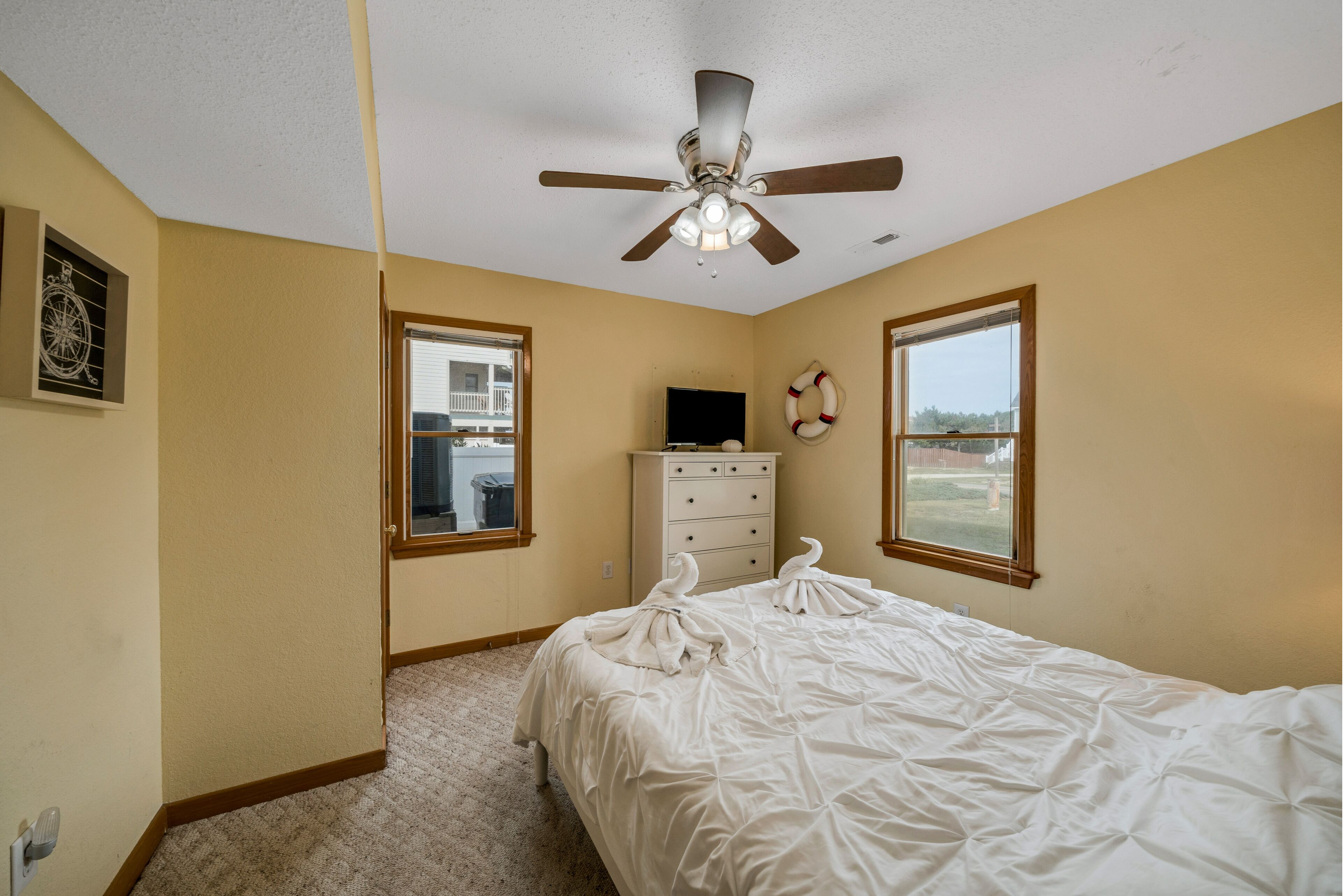 A bedroom with a bed, a ceiling fan, a dresser, and two windows.