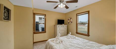 A bedroom with a bed, a ceiling fan, a dresser, and two windows.