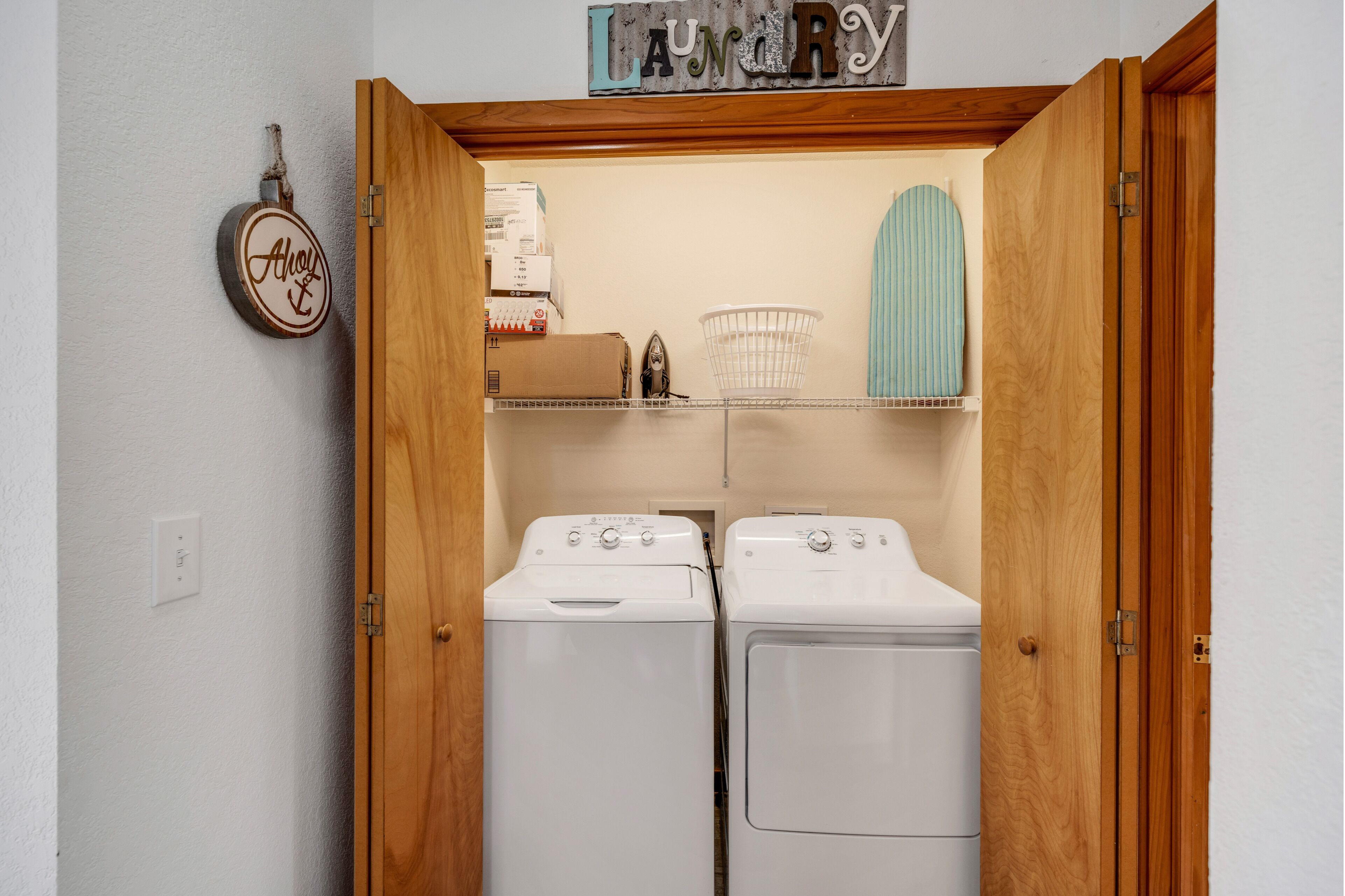 A laundry room with two white washing machines, a wooden door, a laundry basket, and a sign above the machines.