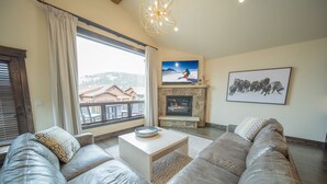 Ein Wohnzimmer mit einer großen Ledersofa, Kamin, Fernseher und Blick ins Freie.
