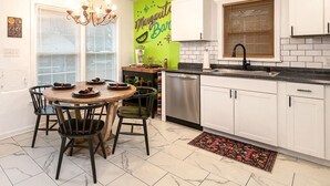 A modern kitchen with white cabinets, a dining table with chairs, a chandelier, and a green accent wall.