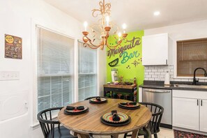 A kitchen with a dining table, chairs, a chandelier, a green wall with a sign, and a window with blinds.
