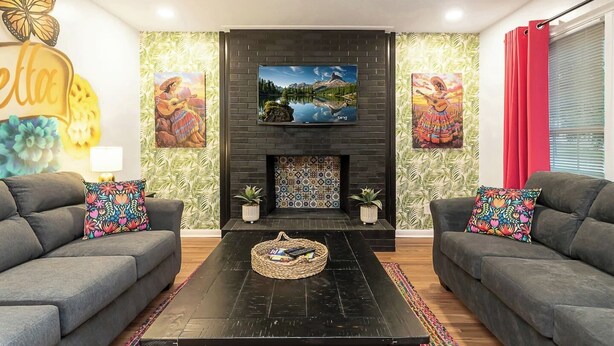 A living room with two grey sofas, a black coffee table, a fireplace with a tiled surround, and a flat-screen TV mounted above the fireplace.