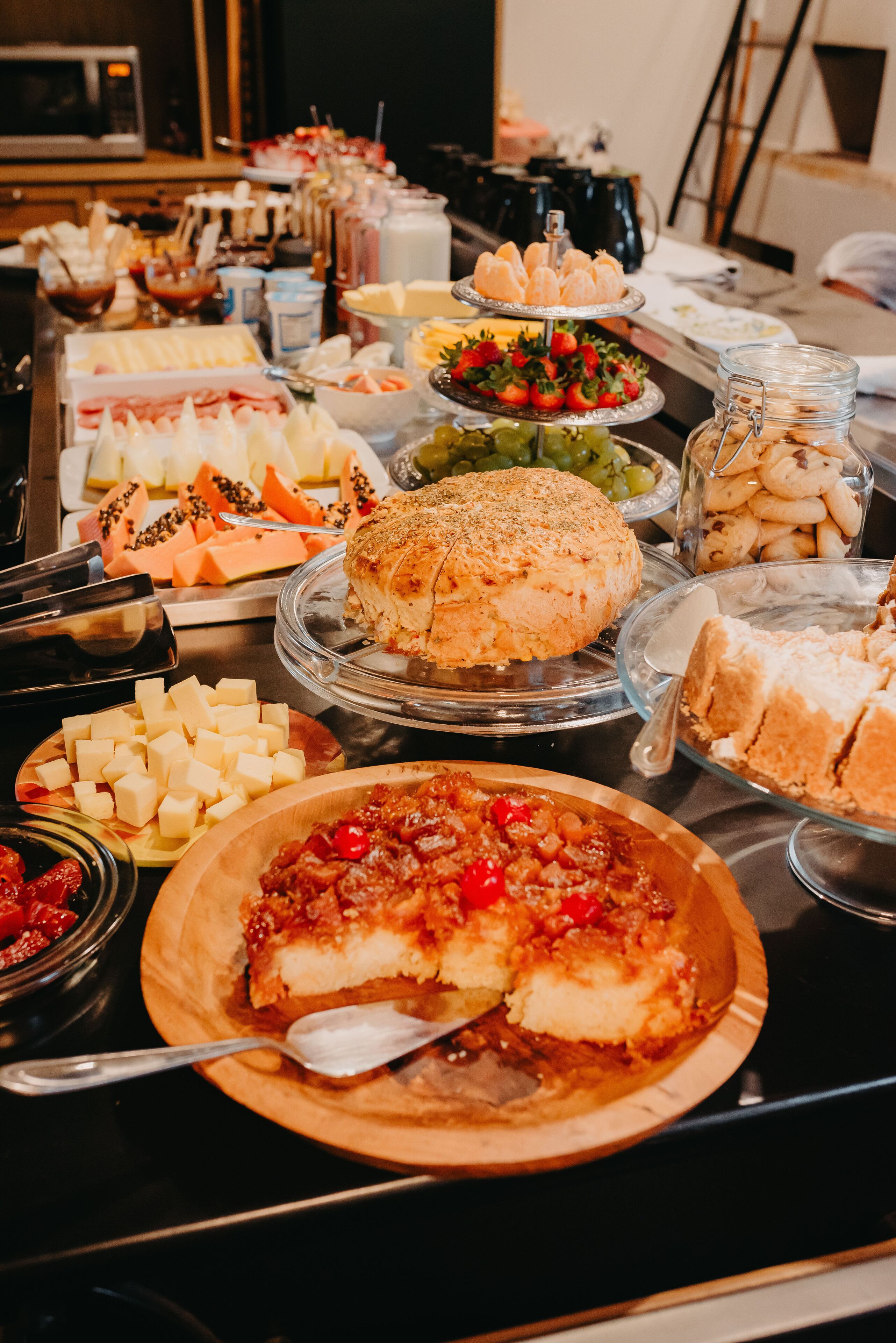 Una mesa de bufé con diversos alimentos, entre ellos queso, frutas y repostería.