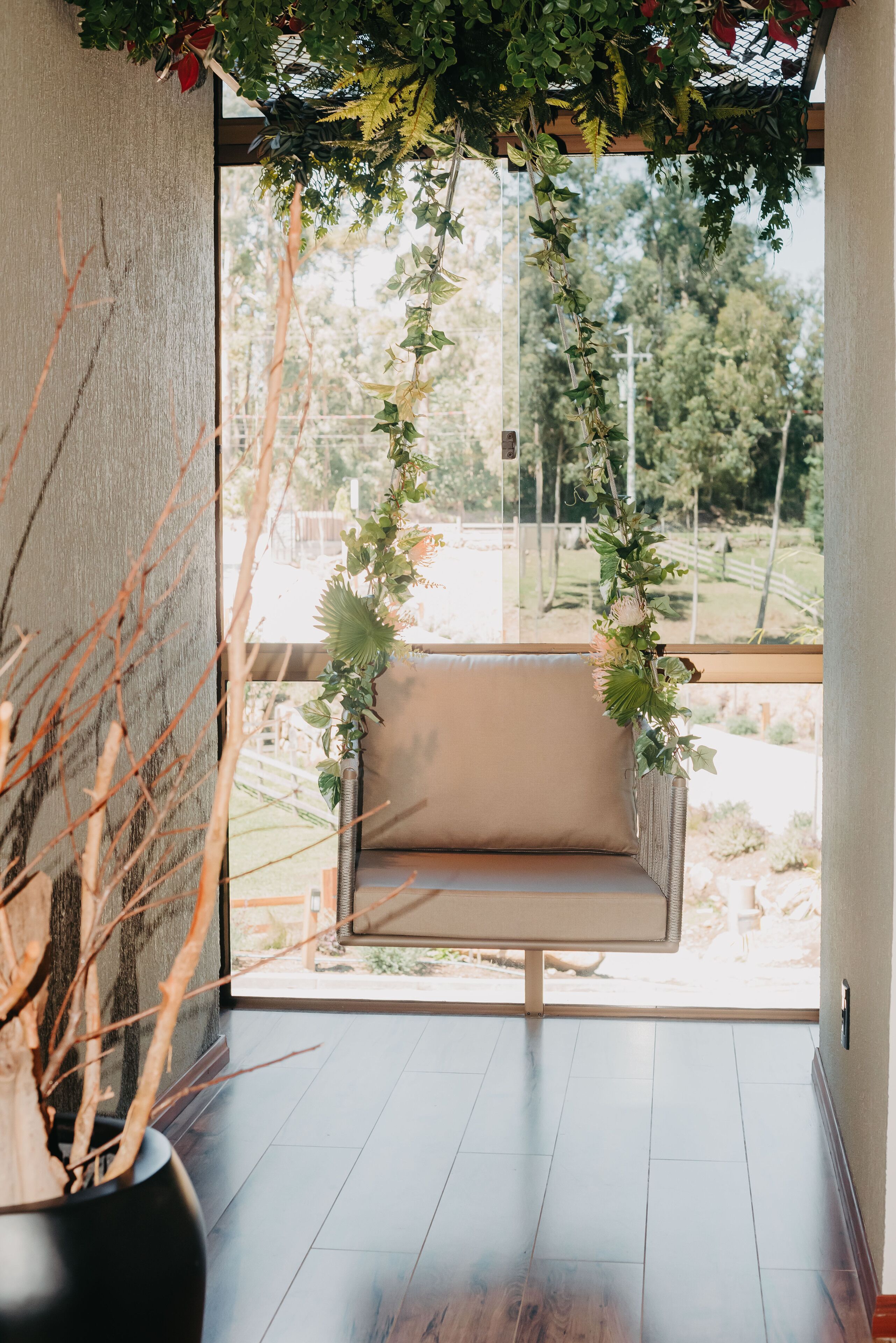 A room with a hanging swing chair, a potted plant, and a view of the outdoors.
