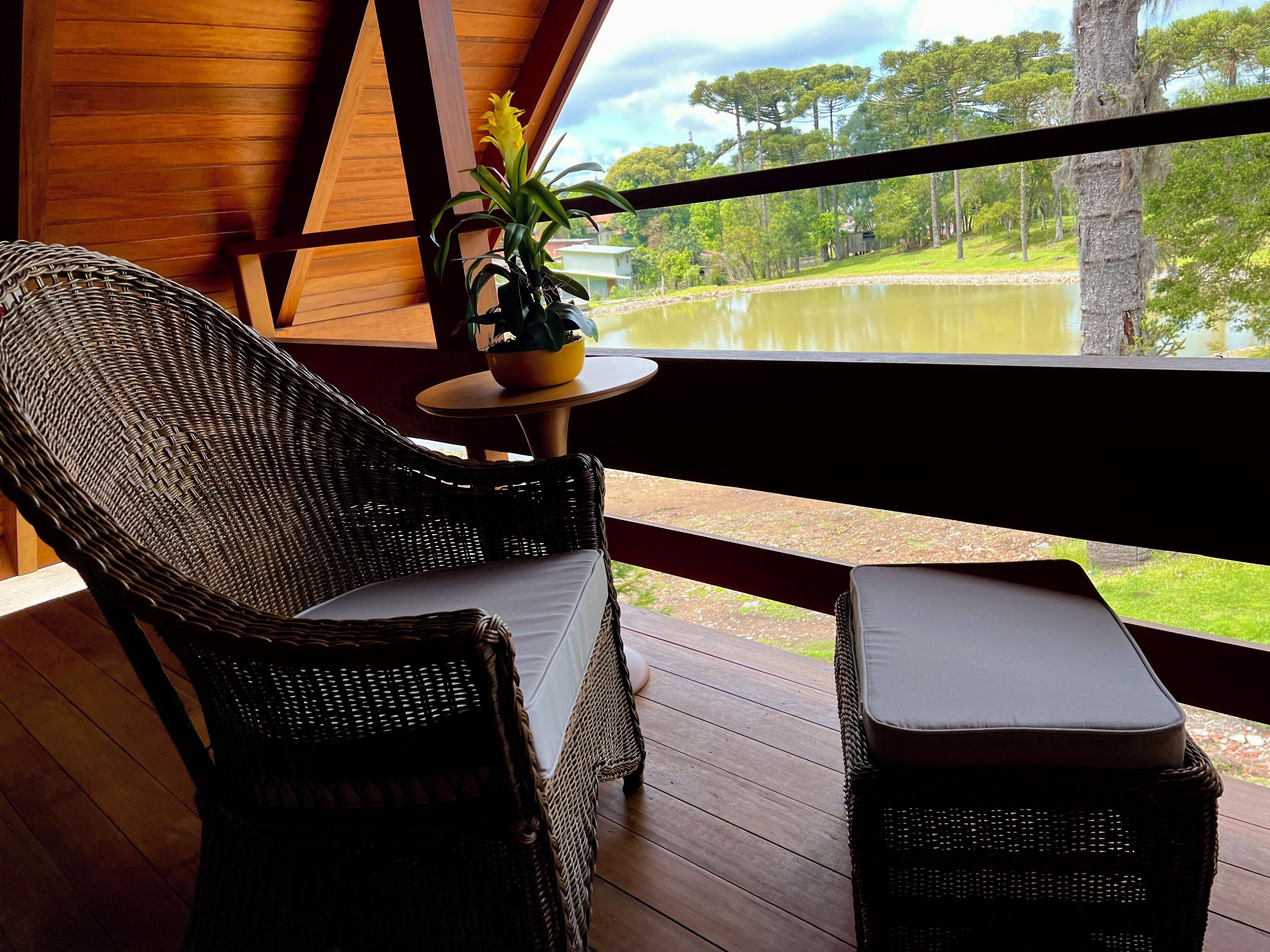 A wicker sofa and table on a wooden deck with a view of a lake and trees.