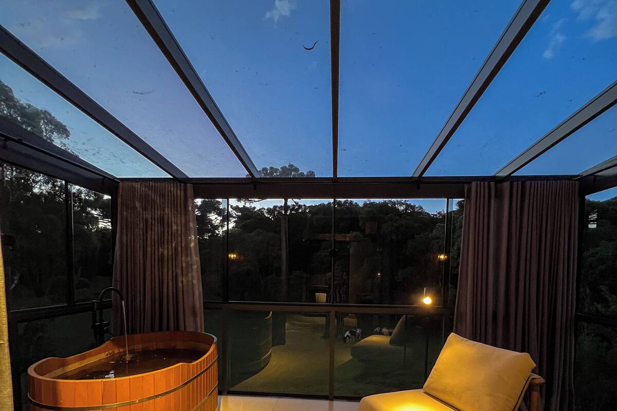 A modern interior with a glass ceiling, a wooden hot tub, and a sofa with a side table.