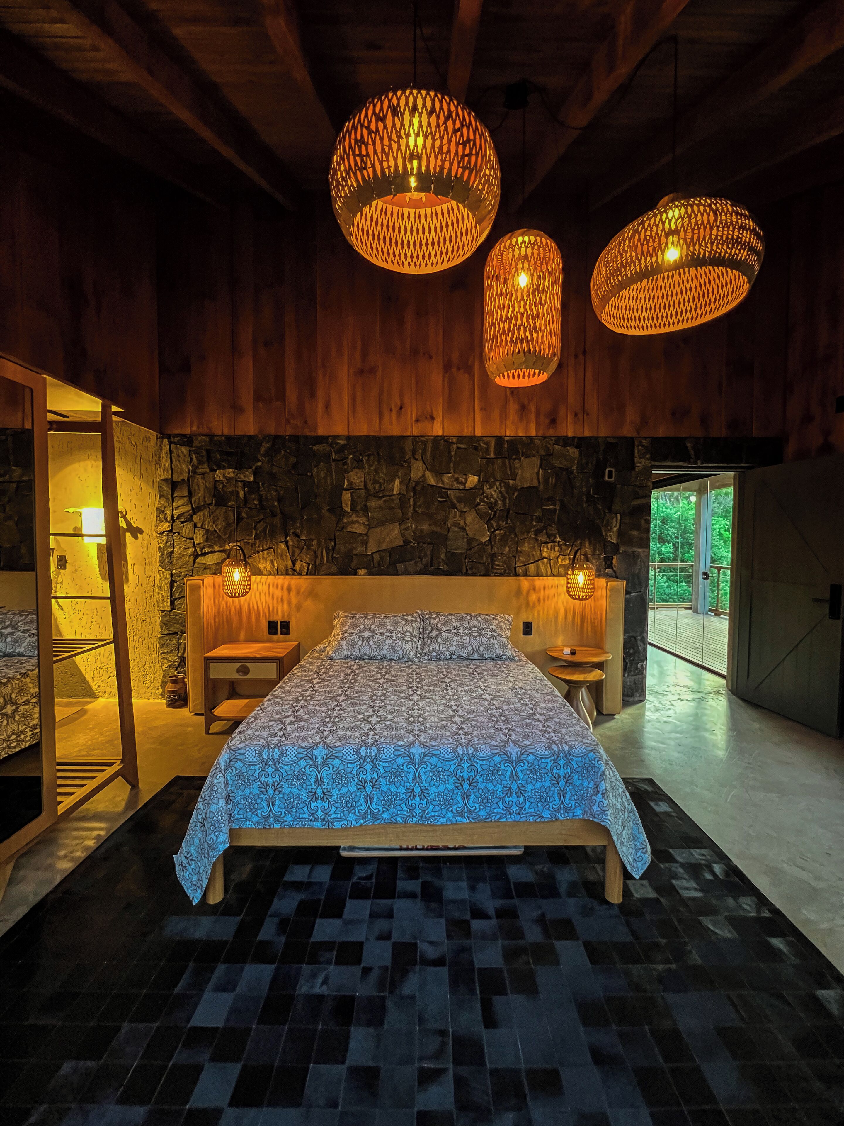 A modern bedroom with a large bed, two wall-mounted lamps, a stone wall, and a wooden ceiling.