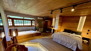 A modern bedroom with a large bed, a sitting area, and a wooden ceiling. - WoodStone Hotel Fazenda (Gramado)
