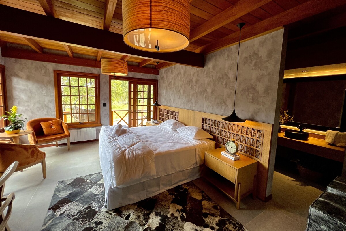 A bedroom with a large bed, wooden headboard, bedside tables, a clock, and a view through a window.