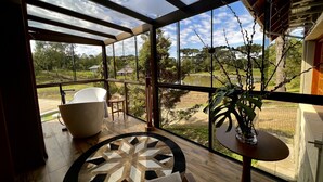 A spacious balcony with a large bathtub, a round table, and a potted plant. - WoodStone Hotel Fazenda (Gramado)