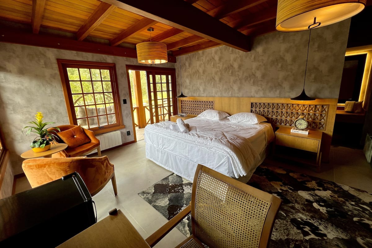 A bedroom with a large bed, a wooden headboard, a bedside table, and a window with a view.