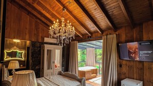 A cozy room with a wooden ceiling, a bed with a wooden headboard, a chandelier, a television, and a view of the outdoors. - WoodStone Hotel Fazenda (Gramado)