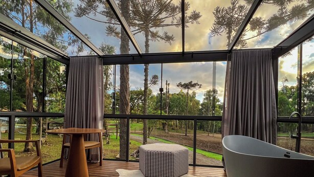 A modern outdoor deck with a wooden floor, a round table, two chairs, a large ottoman, and a bathtub. - WoodStone Hotel Fazenda (Gramado)