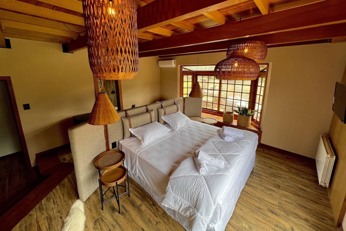 A bedroom with a large bed, wooden beams, and woven light fixtures.