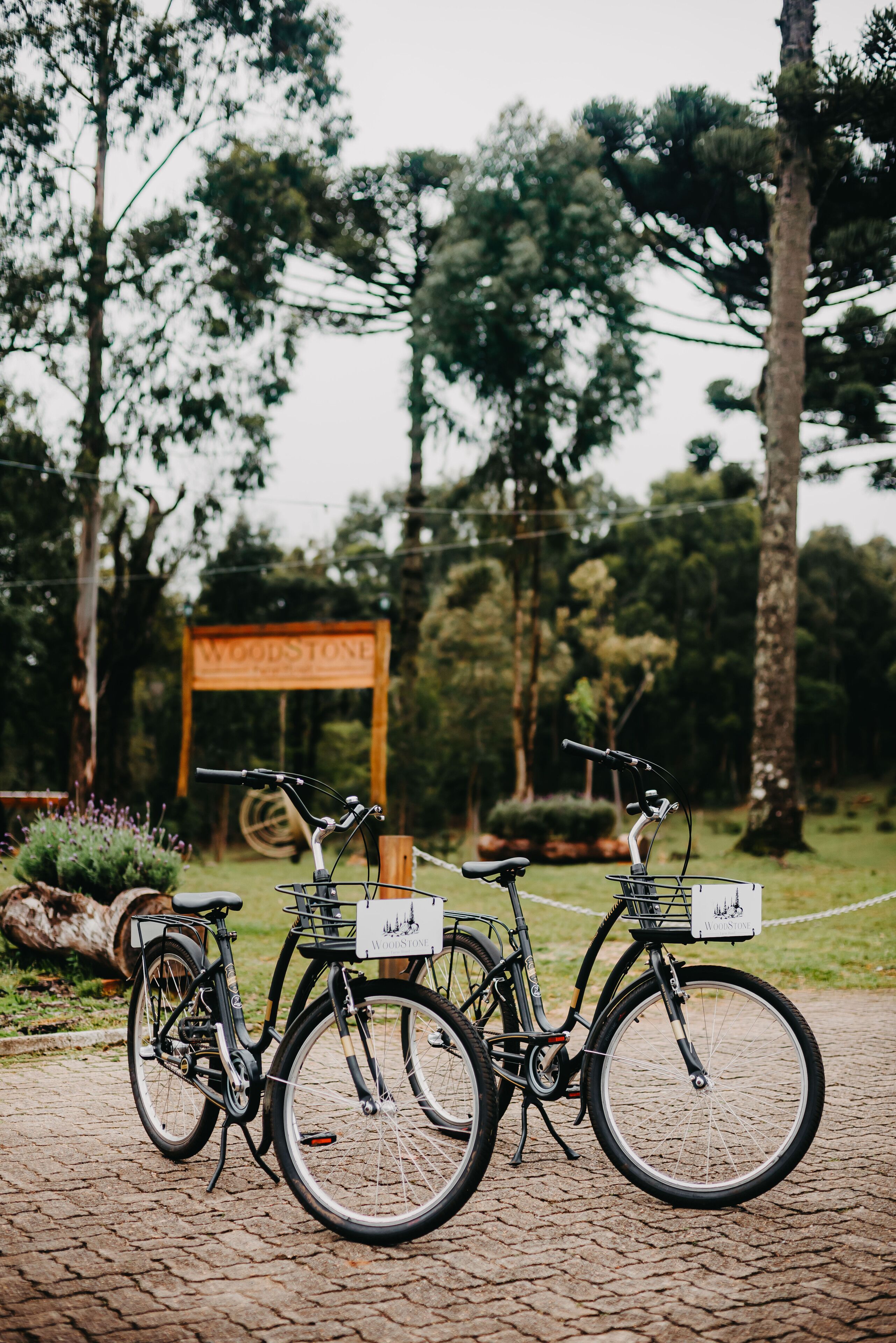 Three bicycles parked on a cobblestone path with a wooden sign in the background.