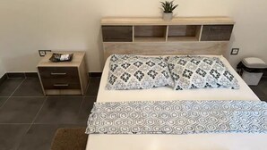 A hotel room with a bed, bedside table, and a small potted plant on the headboard. - Lovely homestay hotel room, 10 minutes from the beach! (Cayenne)