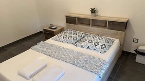 A neatly made bed with patterned bedding and folded towels, a bedside table with a lamp, and a small plant on the headboard. - Lovely homestay hotel room, 10 minutes from the beach! (Cayenne)