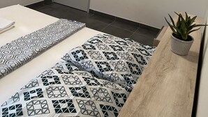 A small, modern room with a bed, a bedside table with a potted plant, a door with a control panel, and an air conditioning unit. - Lovely homestay hotel room, 10 minutes from the beach! (Cayenne)
