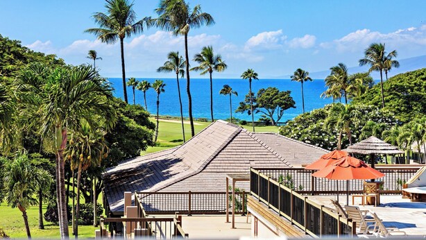 A resort with a pool area, wooden deck, and a view of the ocean.