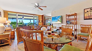 A spacious dining area with wicker furniture, a glass table, and a view of the ocean.