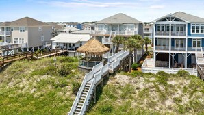 A beachfront property with multiple-story buildings, a wooden deck, and a thatched-roof structure. - Oceanfront Luxury Home with Incredible Panaramic Views & Elevator (Ocean Isle Beach)