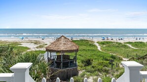 A beach view with a thatched hut, sandy beach, and ocean. - Oceanfront Luxury Home with Incredible Panaramic Views & Elevator (Ocean Isle Beach)