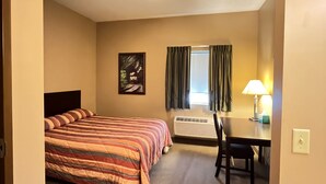 A hotel room with a bed, a desk, a chair, an air conditioning unit, and a window with curtains. - Ambridge Inn (Ambridge)