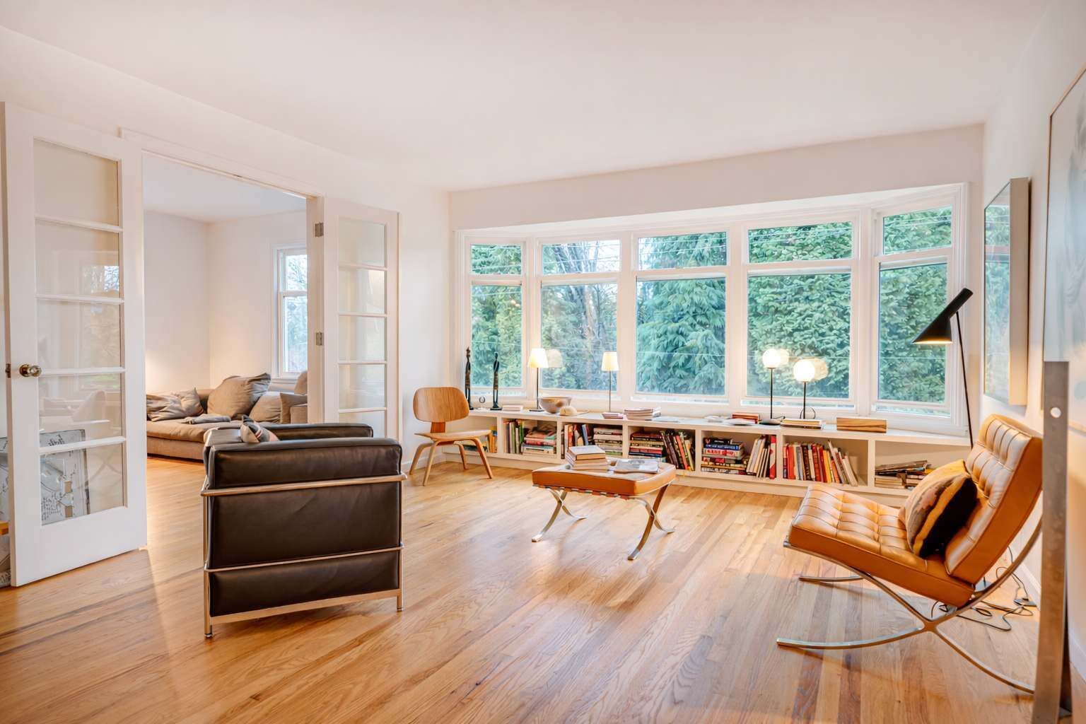 A spacious living room with a large window, a sofa, a chair, a coffee table, and a bookshelf.