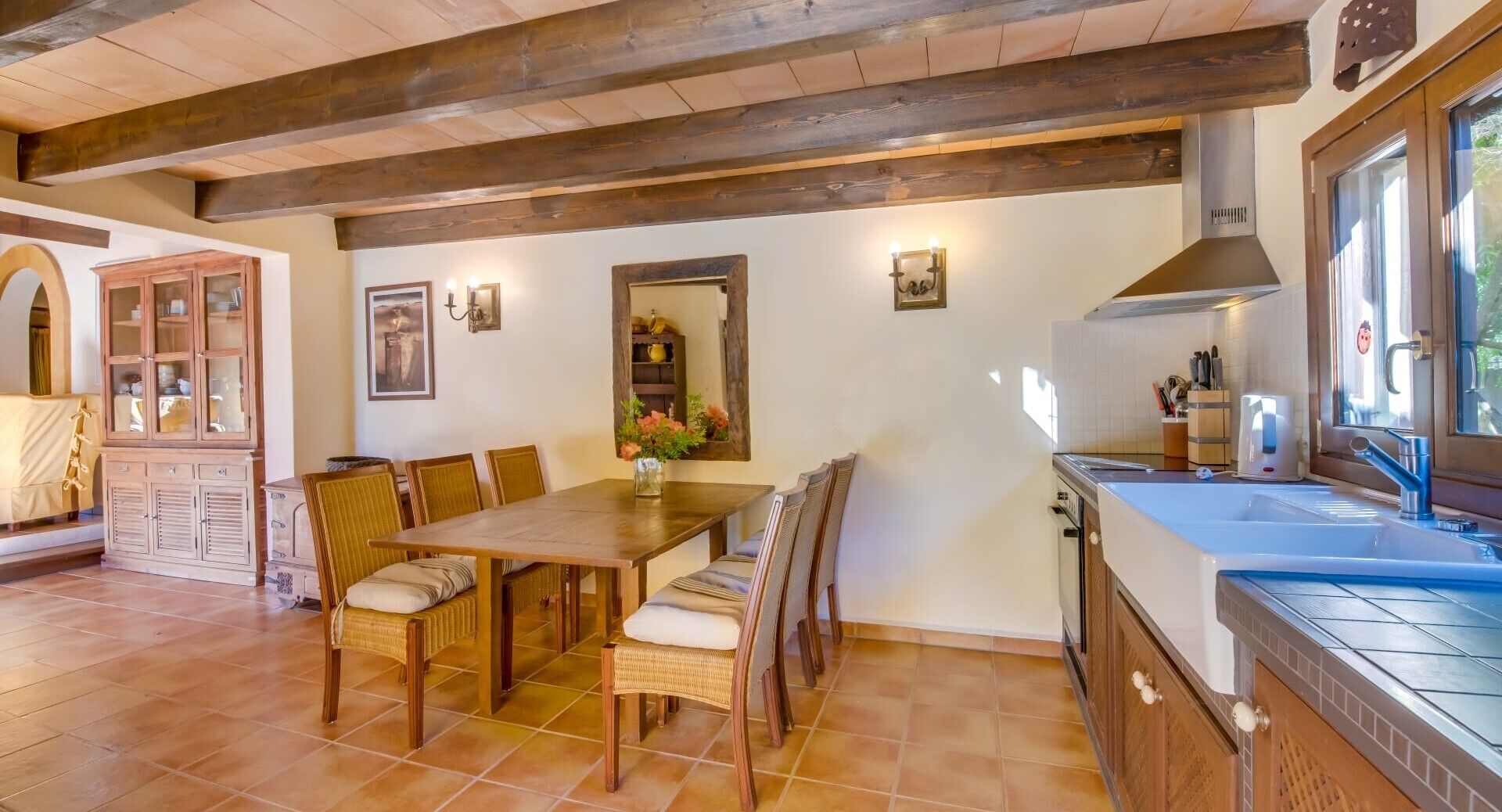 A dining area with a wooden table and chairs, a kitchen with a sink and stove, and a cabinet with glass doors.