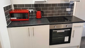 A kitchen with white cabinets, a black countertop, a red microwave, a black electric kettle, and a built-in oven. - Immaculate 3-bed Studio in Liverpool City Centre (Liverpool)